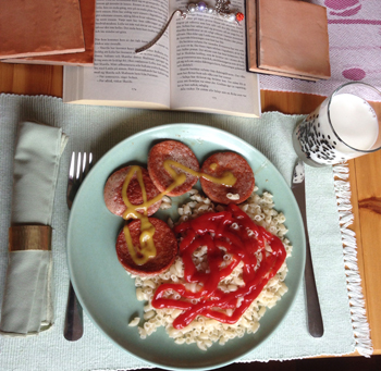 En tallrik med korv, makaroner och ketchup, ett glas mjölk och en uppslagen bok. Kycklingkorv o makaroner
