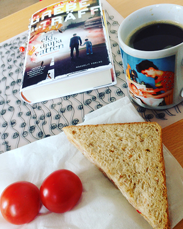 Lunch med smörgås kaffe tomater och bok