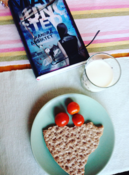 Knäcke och körsbärstomater på en grön assiett, ett glas mjölk och boken Det andra ansiktet av Mari Jungstedt Knäcke tomater mjölk och bok
