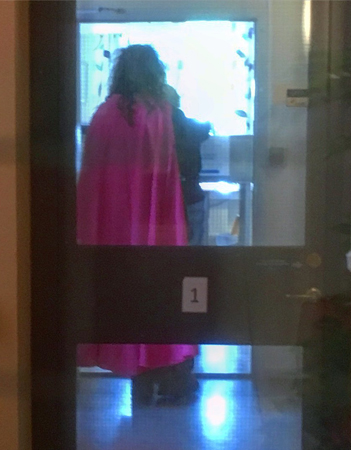 Baksidan av en person med lockigt hår och en rosa cape di Leva