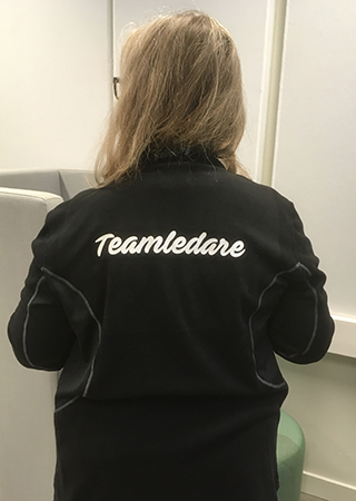 Kvinna i svart jacka med texten "Teamledare" i vitt tryck Teamledare