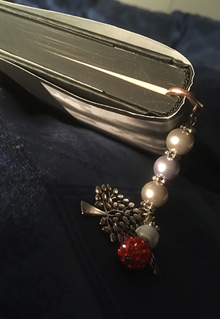 Bok med svarta blad och ett bokmärke med pärlor och en röd ängel