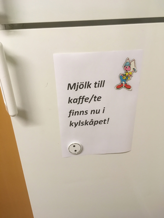 Skylt på kylskåp med texten: "Mjölk till kaffe/te finns nu i kylskåpet!"