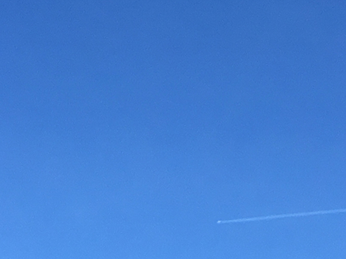 Blå himmel med lite svag rök från ett flygplan