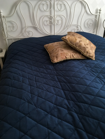 Säng med blått överkast och två guldkuddar