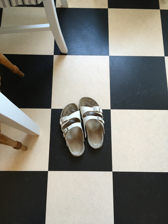 Vita sandaler på rutiga köksgolvet Vita sandaler på rutiga köksgolvet