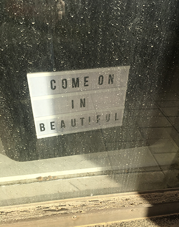 Skylt innanför smutsigt fönster med texten: Come on in beautiful