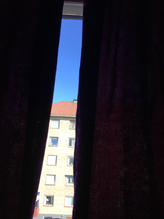 Blå himmel skymtar mellan gardinerna