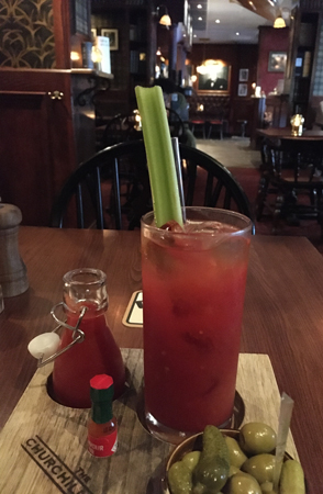 Bloody Mary på Churchill Arms med tomatjuice oliver cornichons syltlök och tabasco på planka. Stor selleristjälk i glaset.