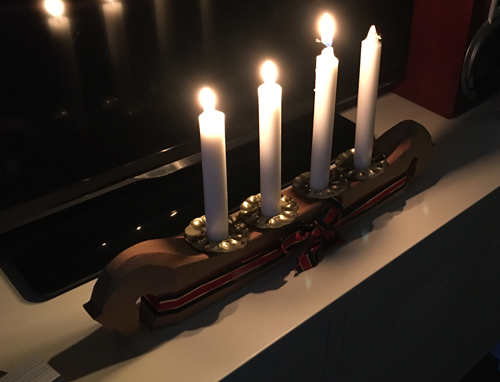 Tredje adventsljuset tänt i adventsljusstaken av trä med hästhuvuden