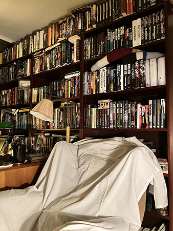 Böcker till höger om sängen och farfarsfåtöljen med lakan i Bokrummet