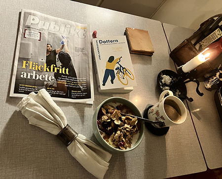 Vardagsfrukost med tänt ljus facktidning och boken Dottern