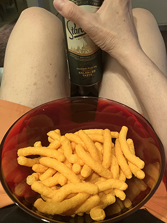 Vita ben i orange shorts med cheddarbågar i röd skål o Staropramen i handen