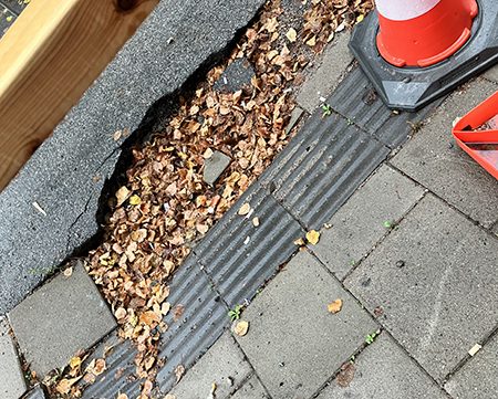 Hål på trottoaren fyllt med höstlöv