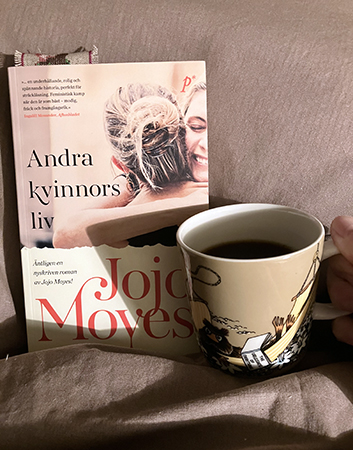 Boken Andra kvinnors liv o kardemummakaffe i brun Muminmugg på sängen