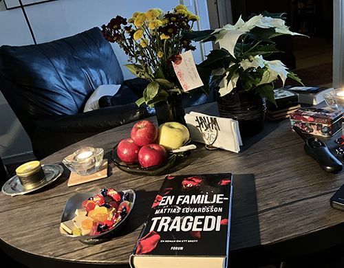 Godisskål o boken En familjtragedi blommor på vardagsrumsbordet