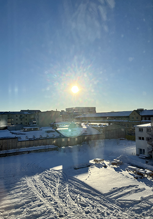 Sol på snöig parkeringsplats fotad genom vardagsrumsfönstret Sol på snöig parkeringsplats fotad genom vardagsrumsfönstret