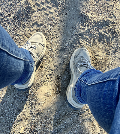 Jeansben och fötter i grå gympadojor på sand