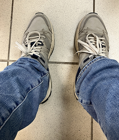 Mina fötter o ben i gympaskor o jeans på klinkergolv