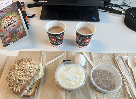 Skrivbordslunch på jobbet med två muggar varm choklad och boken När dolda sorger bleknat