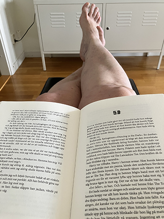 Läser med boken i knäet och ben och fötter på fotpallen