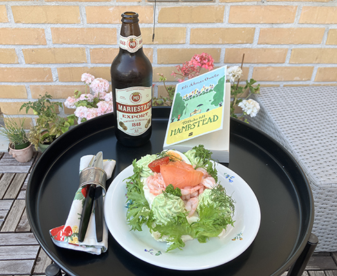 Smörgåstårta och Mariestadöl med boken Tillbaka till Hampstead på balkongen