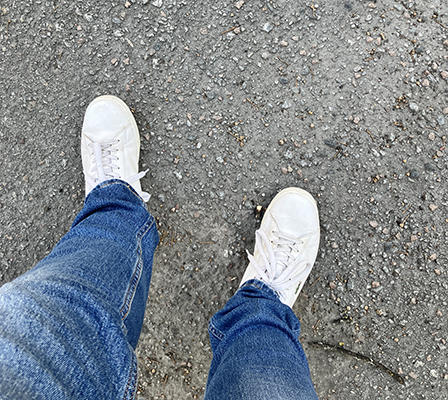 Mina jeansben och vita jympadojor på asfaltspromenad