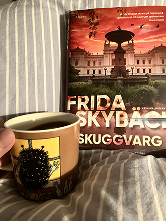 Boken Skuggvarg och kaffe på sängen i muminmuggen Stinky