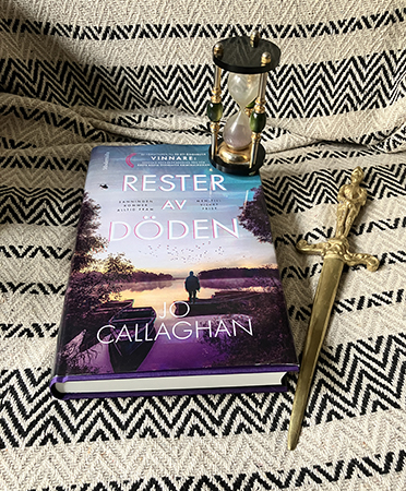 Jo Callaghans bok Rester av döden med timglas och brevkniv i mässing