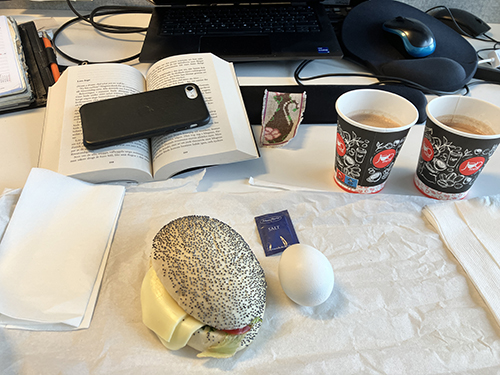 Skrivbordslunch på jobbet med macka ägg varm choklad o uppslagen bok