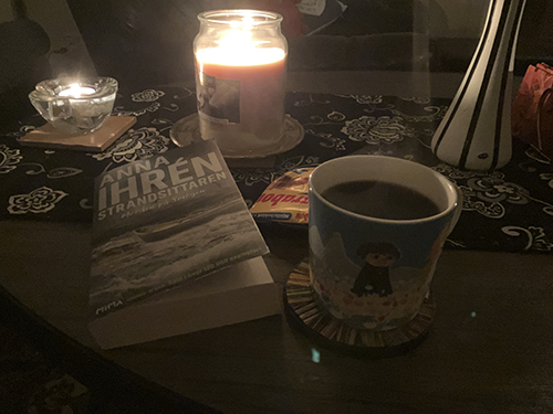 Kvällsfika med boken Strandsittaren choklad kaffe och tända ljus