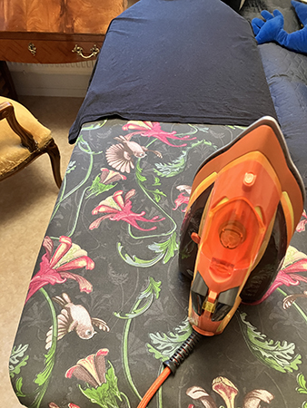 Strykning pågår orange strykjärn och svart tischa på strykbrädan