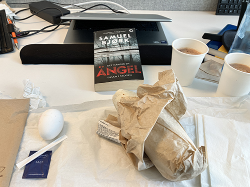 Skrivbordslunch med ägg tonfiskwrap varm choklad o boken Det hänger en ängel ensam i skogen