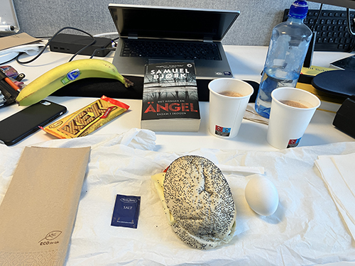 Skrivbordslunch med macka ägg kexchoklad banan varm choklad o boken Det hänger en ängel ensam i skogen