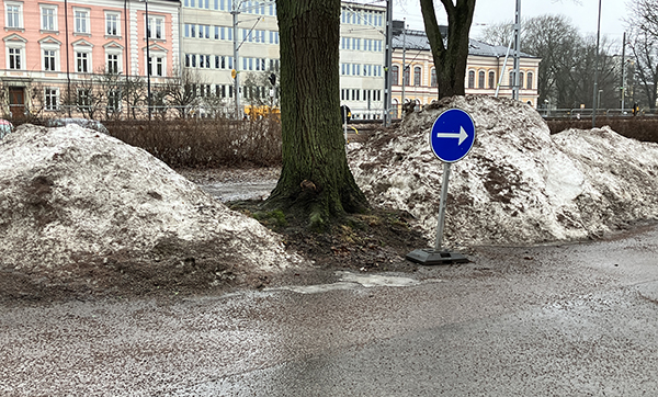 Regnvåt gata med snöhög och skylt med pil Regnvåt gata med snöhög och skylt med pil