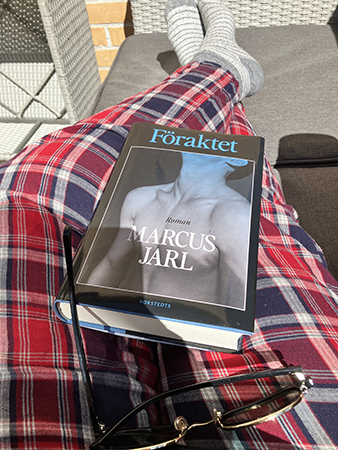 Boken Föraktet och solbrillor i knäet på mig i balkongsoffan
