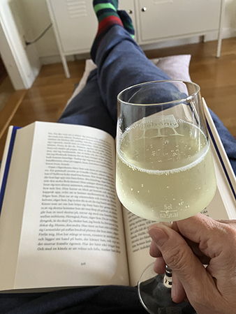 Bokuppslag i knäet och bubbel i glas i handen