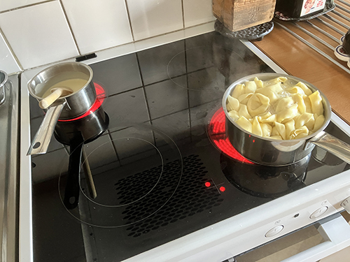 En kastrull med sås och en kastrull med tortelloni på spisen