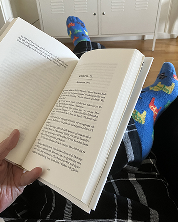 Håller en bok mellan tummen o lillfingret o vänsterbenet över högerbenet Håller en bok mellan tummen o lillfingret o vänsterbenet över högerbenet