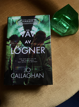 Boken Väv av lögner med grön brevpress på gul sammetsstol
