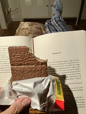 Läser och äter kexchoklad i fåtöljen
