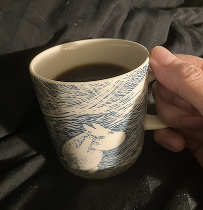Mumin i blåsvädermugg med kaffe på sängen
